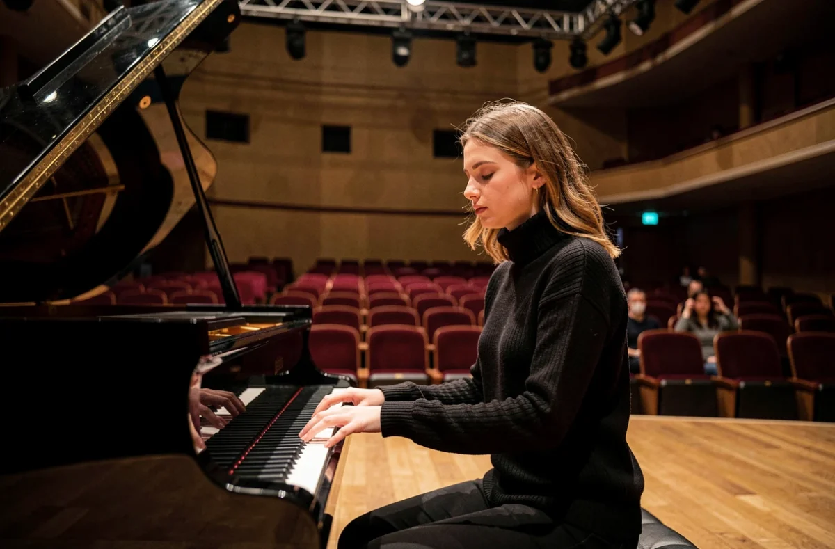 Jeune pianiste française en répétition sur scène dans une salle de concert vide, interprétant un répertoire allant de Debussy à Philip Glass